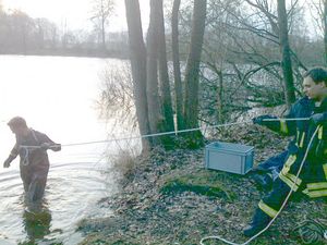 Ein Kamerad - gesichert durch einen weiteren Kameraden - wagt sich in den Teich.