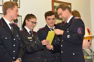 Jugendwart Manfred Köncke überreicht den vollgeschriebenen Jugendfeuerwehrausweis an Leonie.