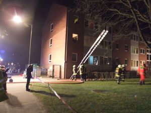 Auf der Vorderseite des Wohnblocks wird eine Steckleiter in Stellung gebracht um Bewohner durch die Fenster zu retten.